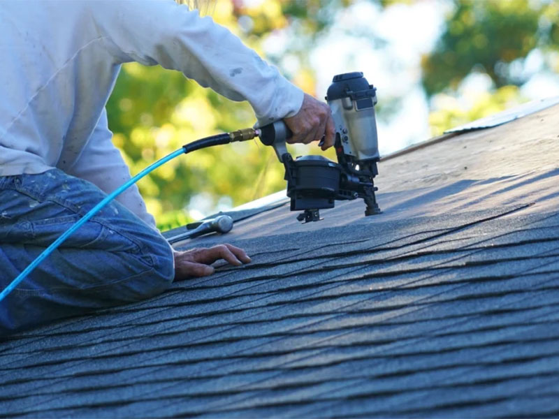 Contractor installing asphalt shingles on a roof.