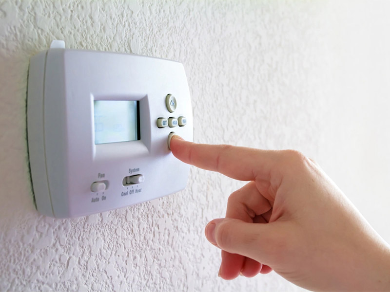 Hand adjusting a home thermostat on a wall.