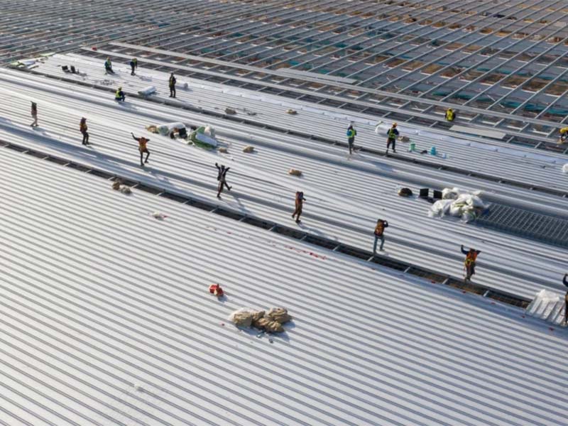 Workers installing metal panels on a large commercial roof