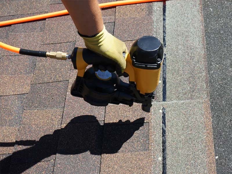 Nail gun being used on asphalt roof shingles.