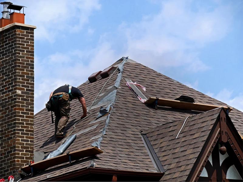 Roofer repairing shingles and flashing near a chimney