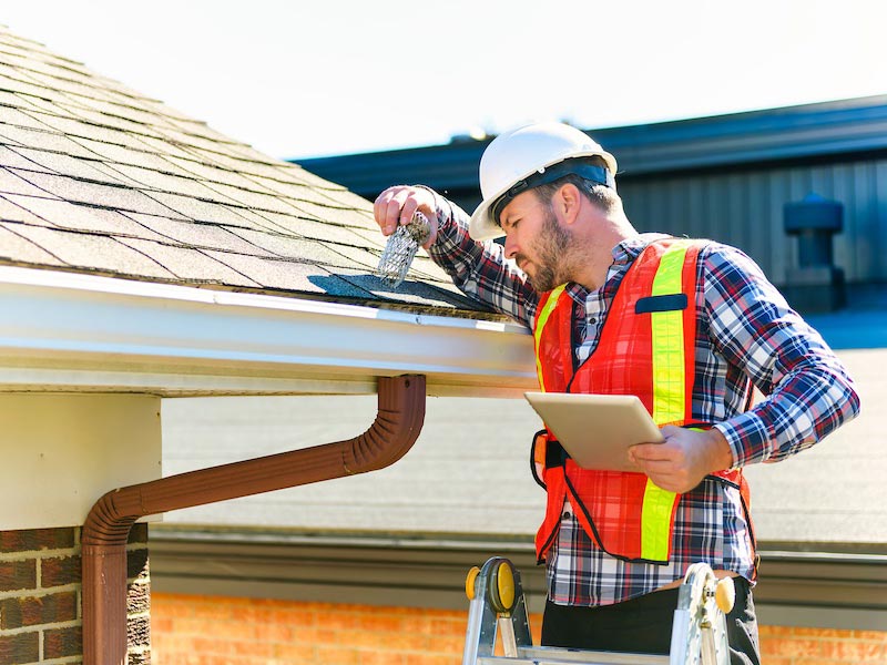 Inspector checking roof shingles near a gutter.