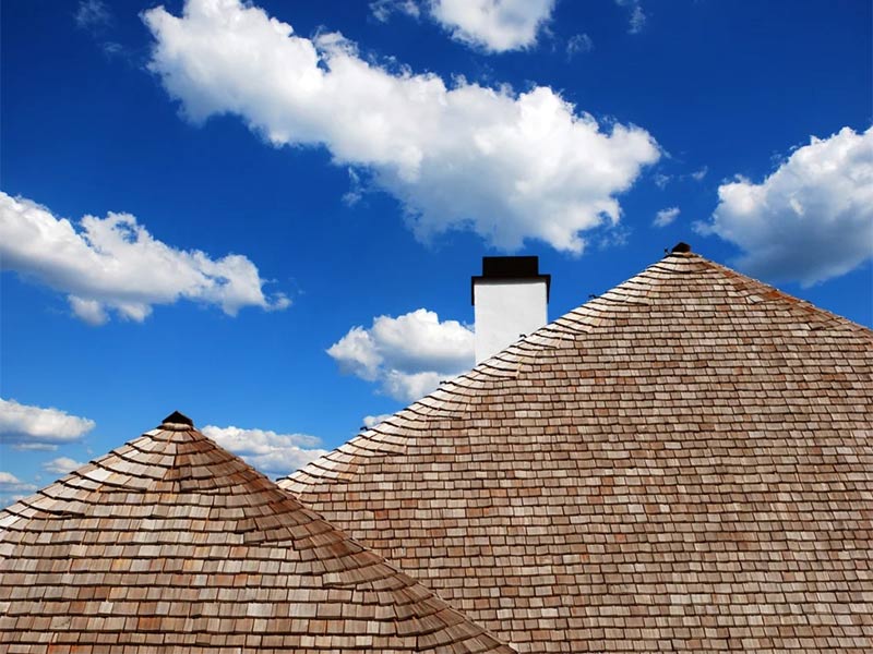 Wood shake roof with chimney under blue sky.