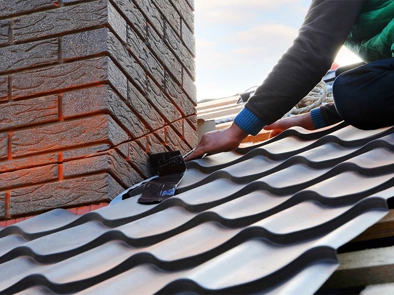 Worker installing metal roof tiles near a chimney.