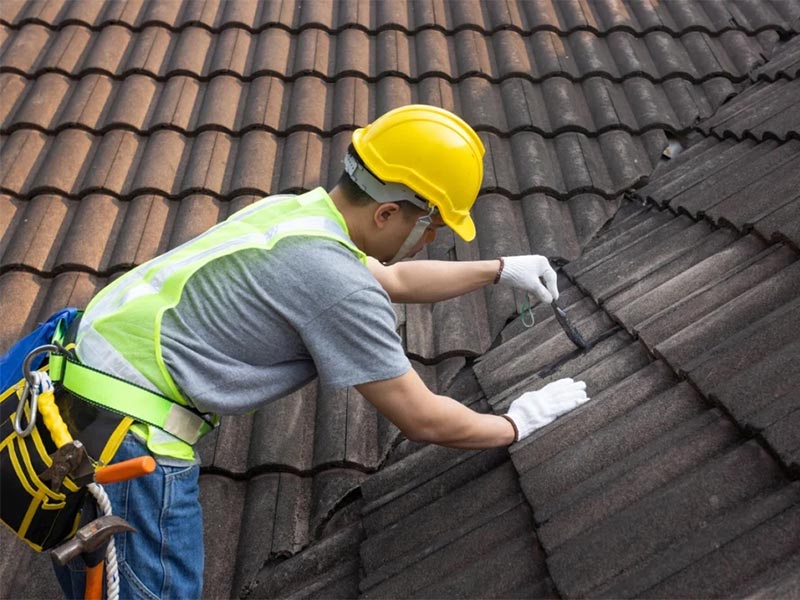 Worker applying waterproof coating on roof tiles.