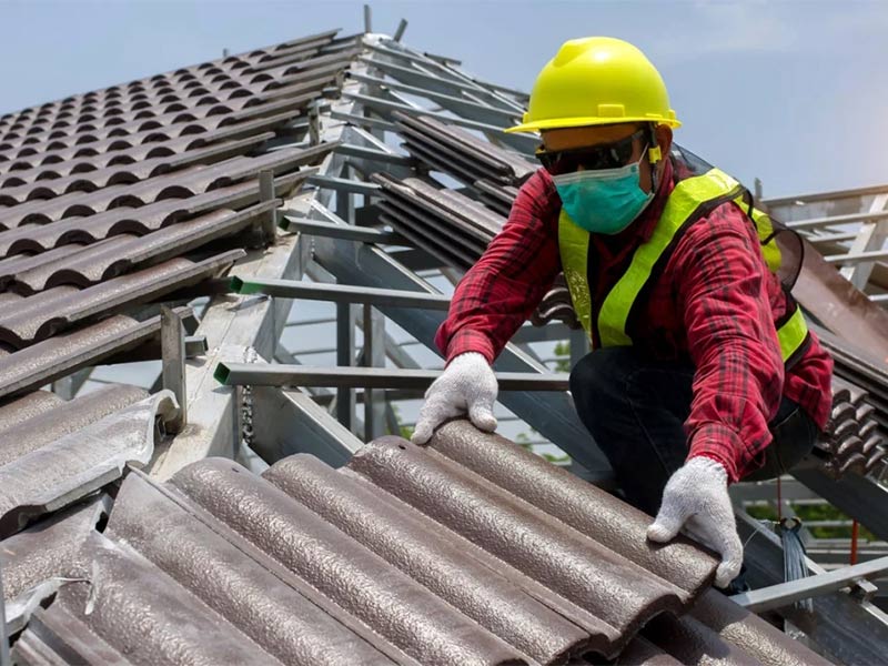 Worker placing roof tiles while wearing safety gear.