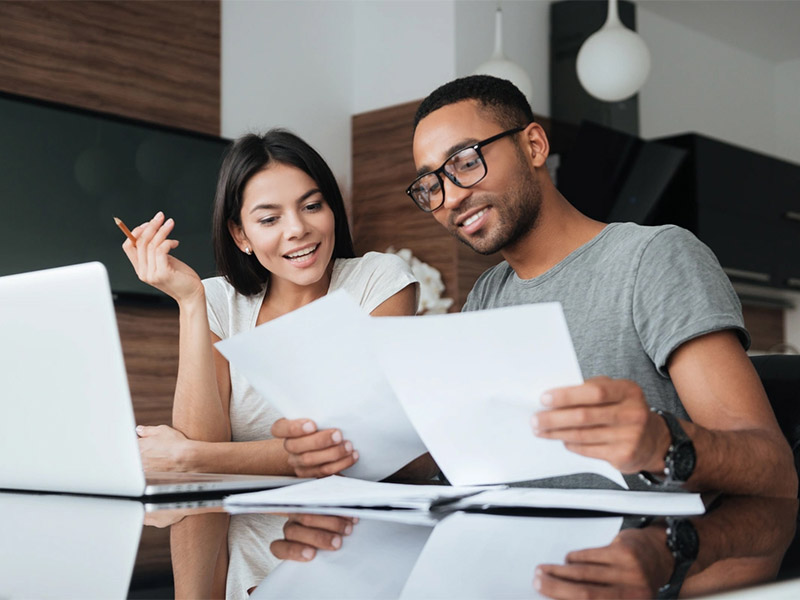 Two people reviewing paperwork at a table with a laptop.